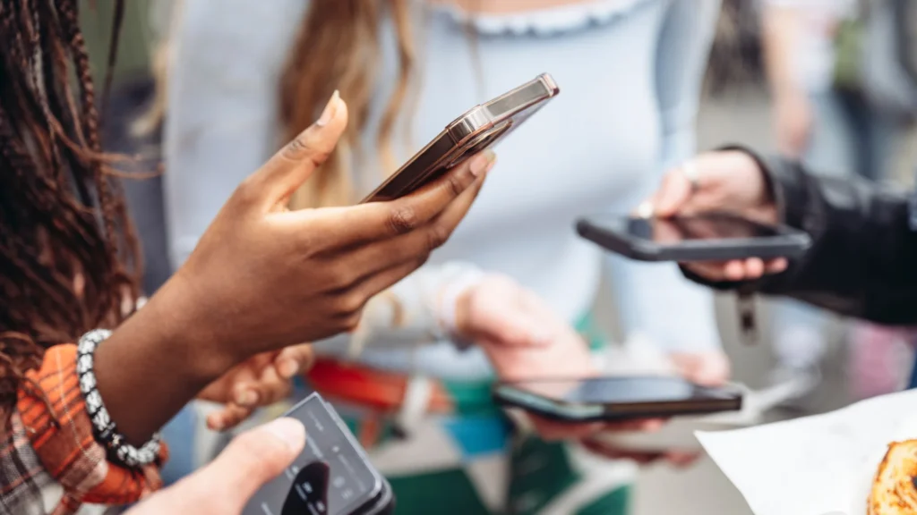 Groupe de jeunes utilisant leurs smartphones, illustrant à quel GAFAM ces réseaux sociaux appartiennent-ils